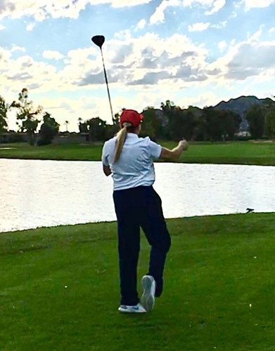 Person swinging a golf club on a grassy course