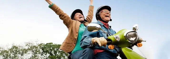 Two people riding a green scooter outdoors with arms raised